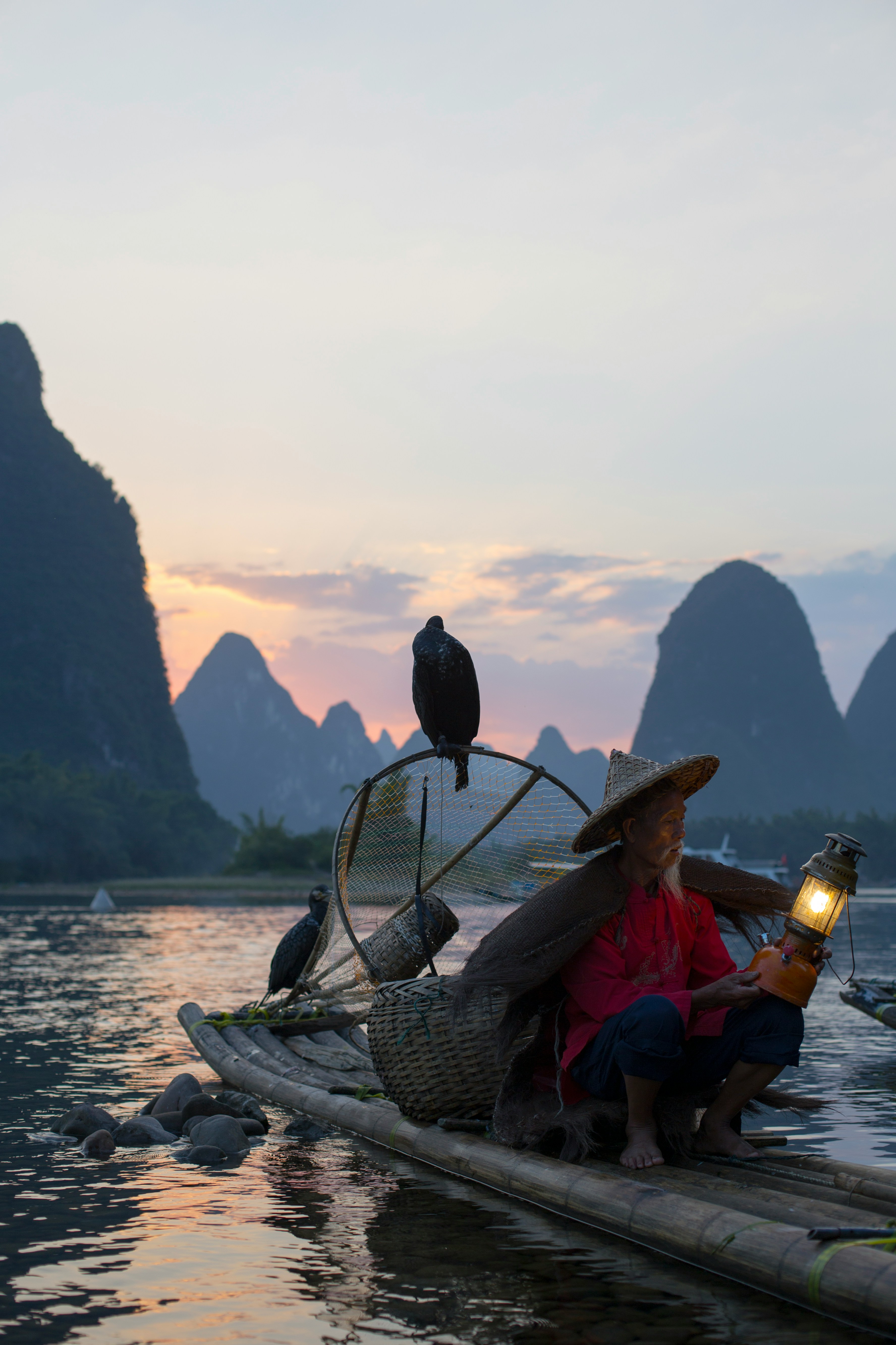 A wise, elderly fisherman with cormorant birds on his bamboo raft at dusk, symbolizing experience, patience, and a deep connection to nature's rhythms.