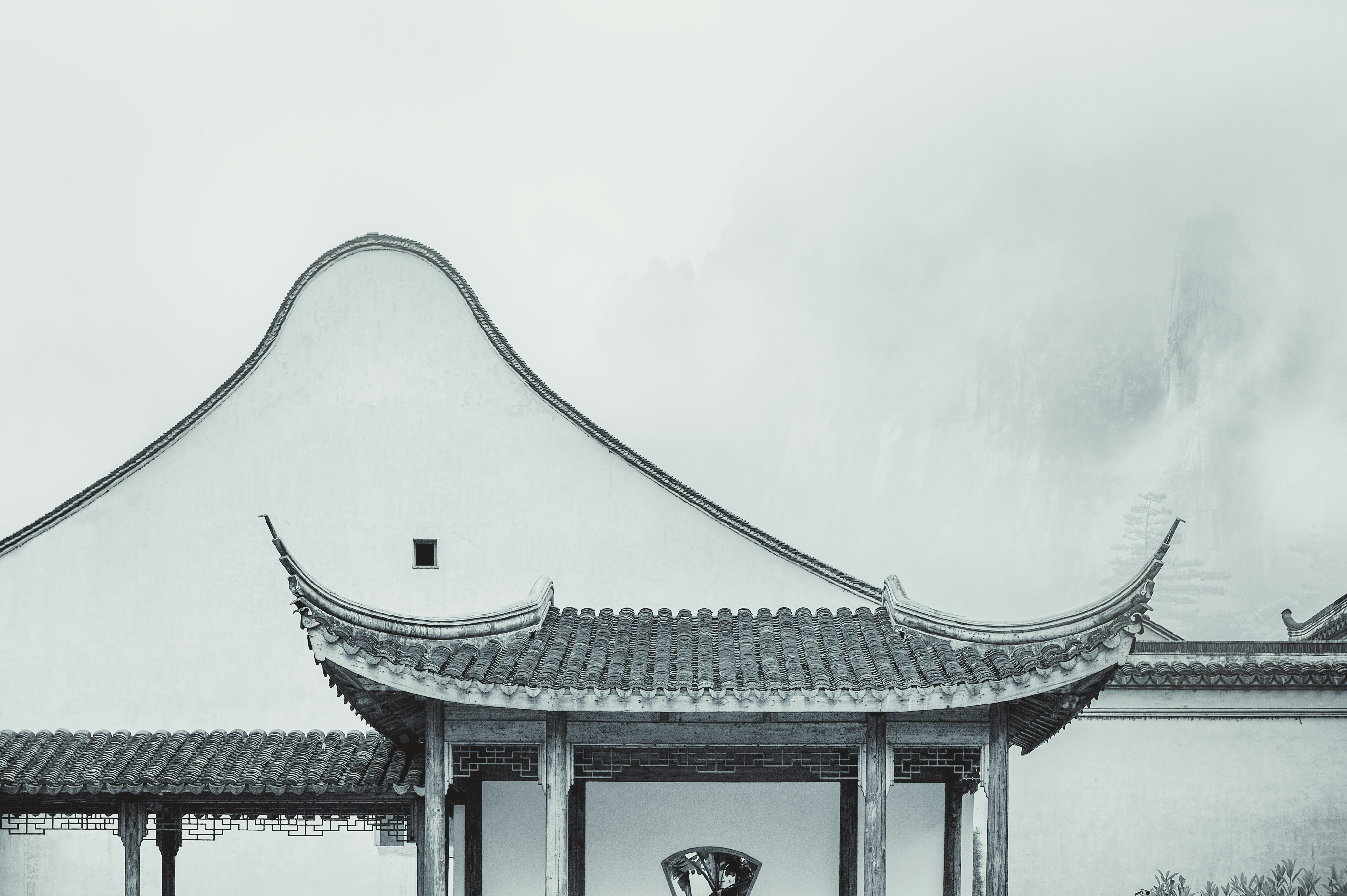 A serene black and white photo of a traditional Chinese pavilion with a curved roof, set against a misty mountain backdrop, evoking a sense of ancient wisdom.